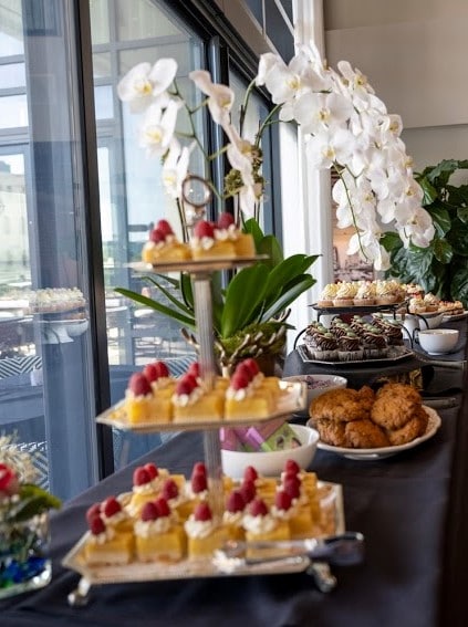 tier trays of mini cakes, cookies, and other desserts in front of large window at wedding reception